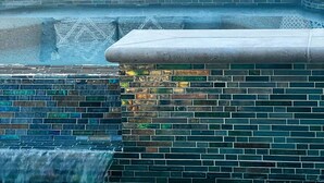 Un espace piscine agrémenté d’un mur carrelé, d’une petite cascade et d’un coin salon avec des coussins.