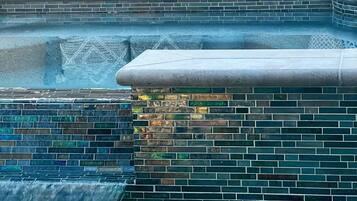 A pool area with a tiled wall, a small waterfall feature, and a seating area with cushions.