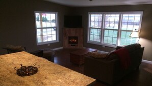 A living room with a fireplace, a television mounted above it, and large windows. - Secluded, Log Rental Cabin, Private Hot Tub,on Southern Illinois Wine Trail (Buncombe)