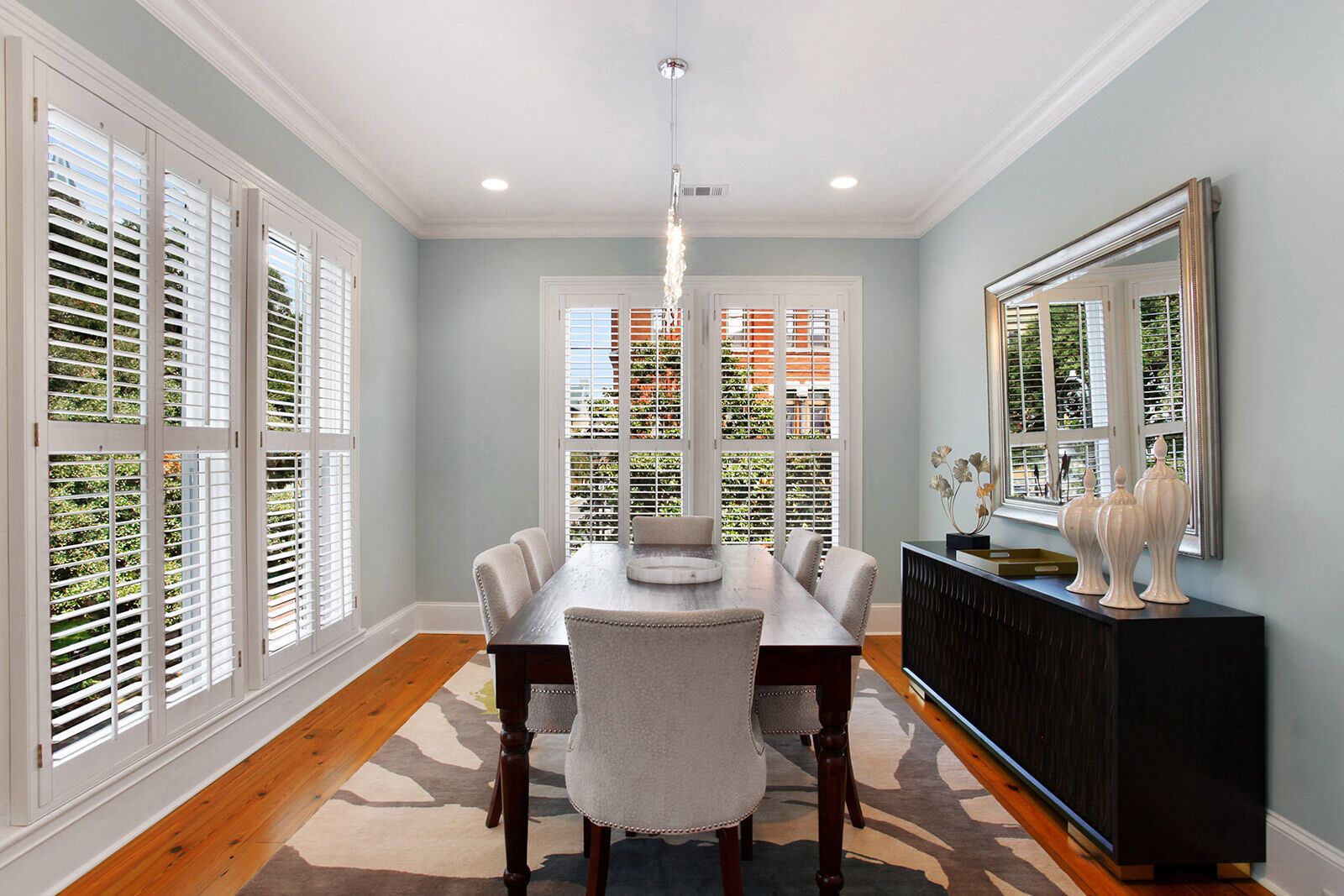 A dining room with a wooden table, six chairs, a chandelier, and a large mirror on the wall.