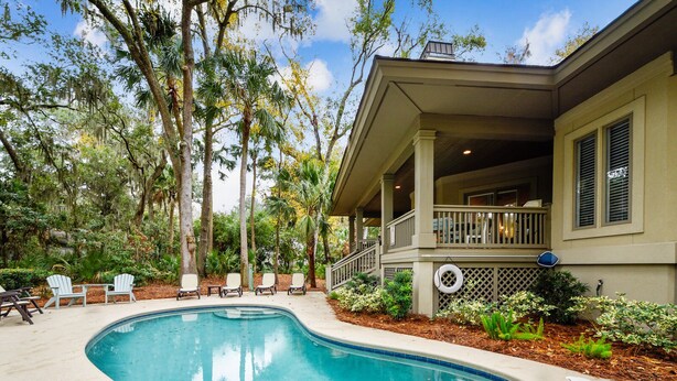 A swimming pool with a curved edge, surrounded by a deck with lounge chairs. - Perfect Family Home w/ Pool & Lagoon Views (Hilton Head Island)