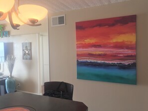 Enjoy a serene atmosphere with a stunning sunset painting and a comfortable dining area.