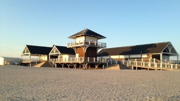 Ein Gebäude direkt am Strand mit mehreren Etagen, einem zentralen Turm und einem überdachten Gang.