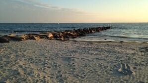 Ein Strand mit einem steinernen Wellenbrecher und klarem, blauem Wasser.
