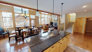 A spacious kitchen with a large island, wooden cabinets, and a view of a mountain cabin through large windows. - Spectacular Mountain Views | Private Hot Tub | Fire Pit | Central A/C (Panorama)