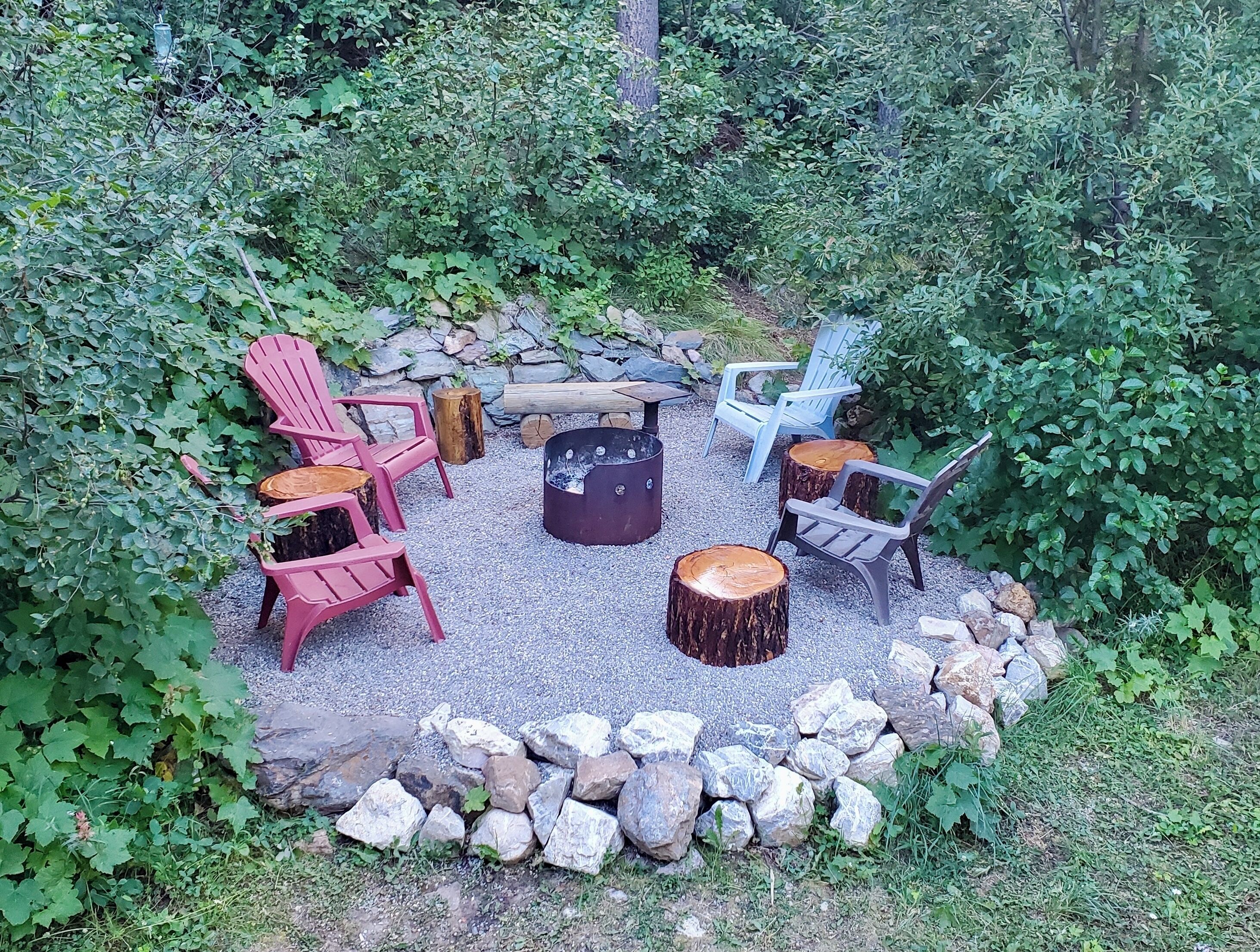 An outdoor seating area with Adirondack chairs, a fire pit, and a stone wall.