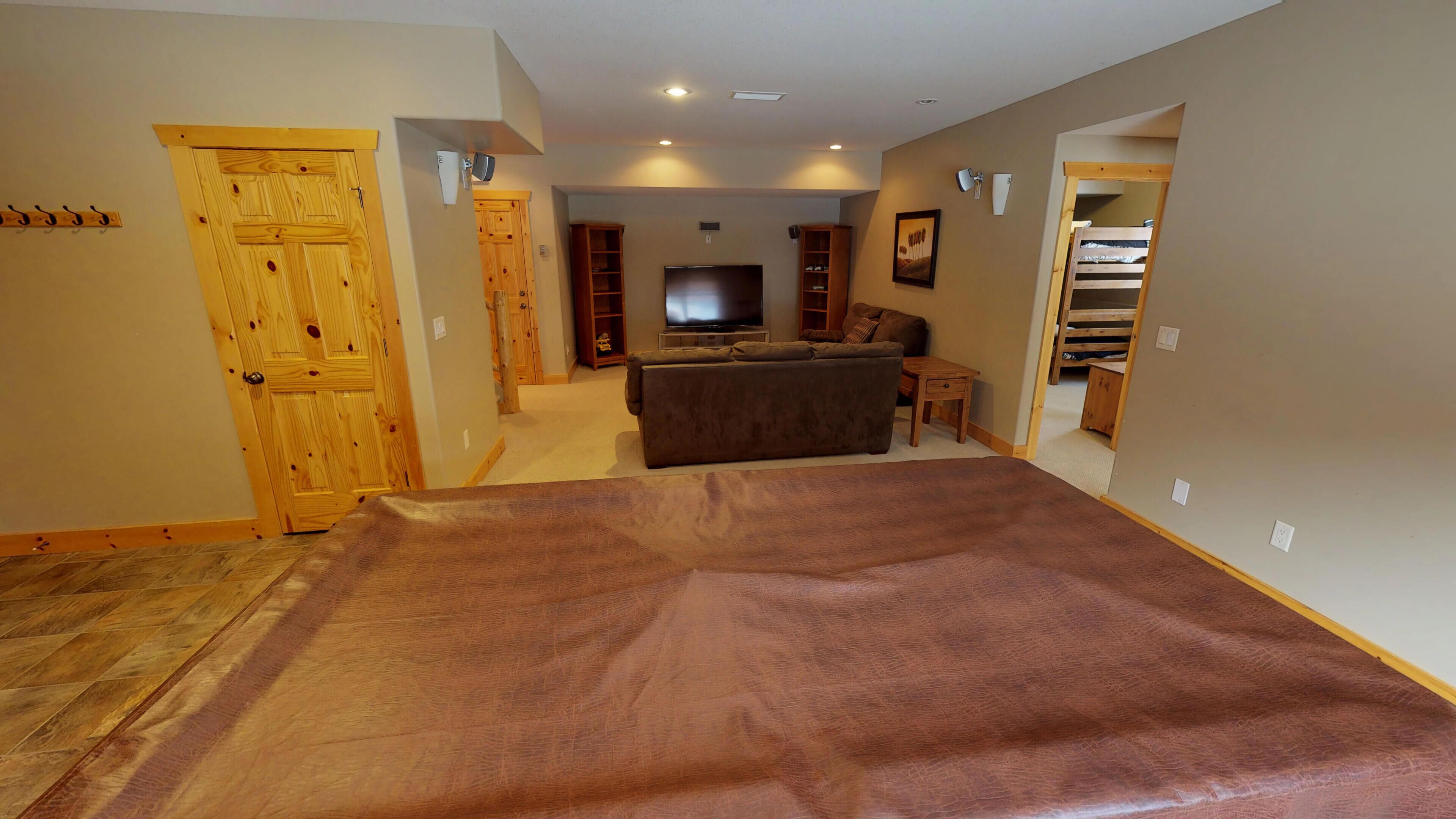 A spacious living room with a large brown carpet, wooden doors, a television, and a sofa.