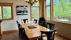 A dining area with a wooden table and chairs, large windows, and a chandelier. - Spectacular Mountain Views | Private Hot Tub | Fire Pit | Central A/C (Panorama)
