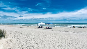 A beach with a white umbrella and beach chairs, a sandy shore, and the ocean in the background.