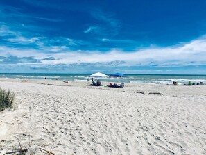 Een strand met een witte parasol en ligstoelen, een zandstrand en de oceaan op de achtergrond.