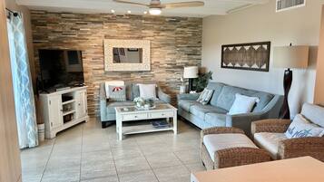 A living room with a stone wall, a ceiling fan, a television, a sofa, a coffee table, and wicker furniture.