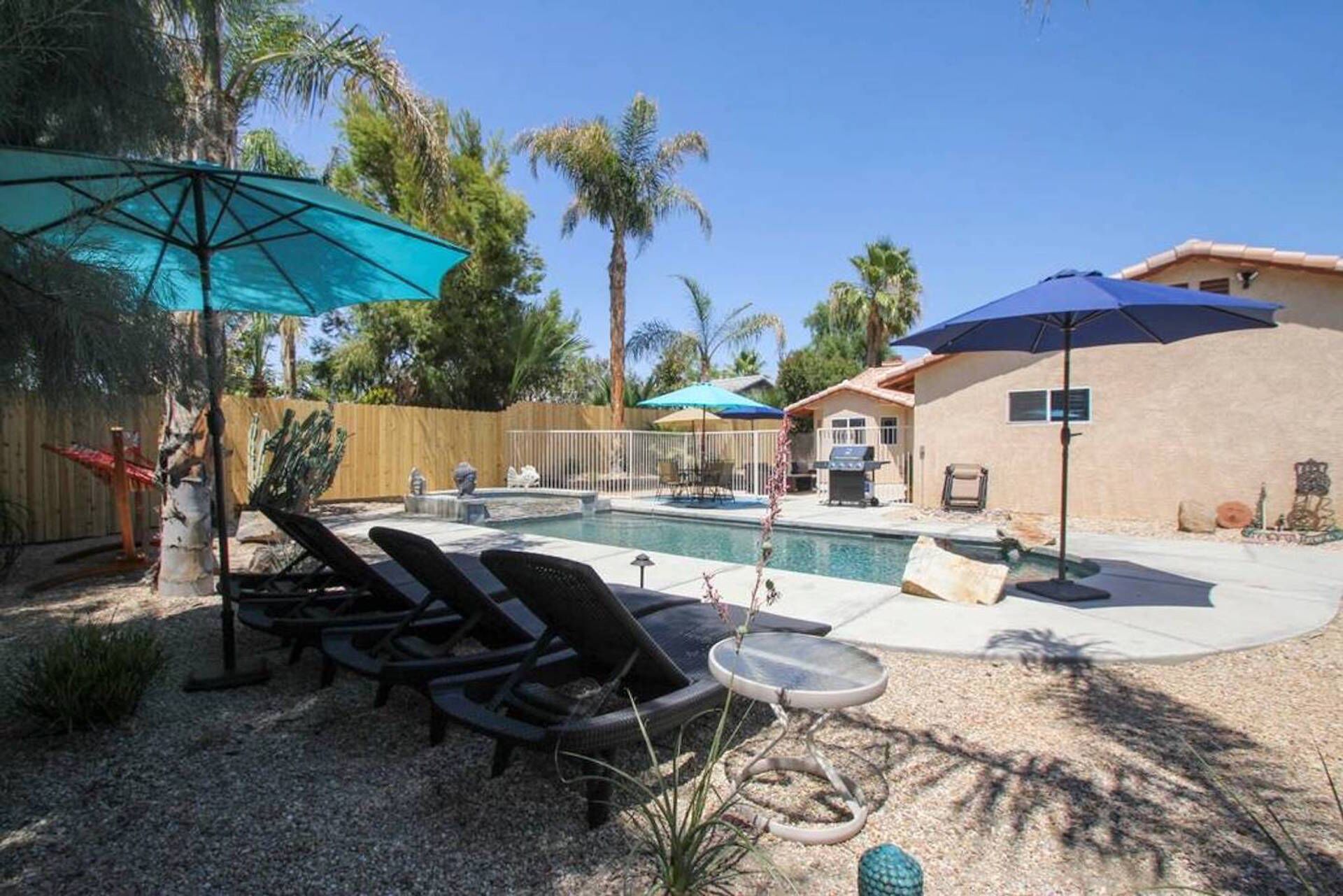 A backyard with a swimming pool, lounge chairs, and umbrellas.
