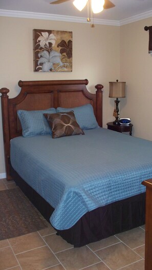 A bedroom with a wooden bed, blue bedding, a nightstand with a lamp, and a wall clock. - Newly Renovated Condo in Beautiful Beach Front Resort (Hilton Head Island)