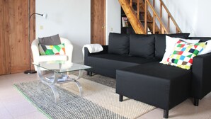 Un soggiorno moderno con un divano nero, una poltrona bianca e un tavolino da caffè in vetro. Sullo sfondo, una scala in legno.