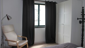 Camera da letto con un letto singolo, una sedia, una lampada da scrivania e una finestra con tende.