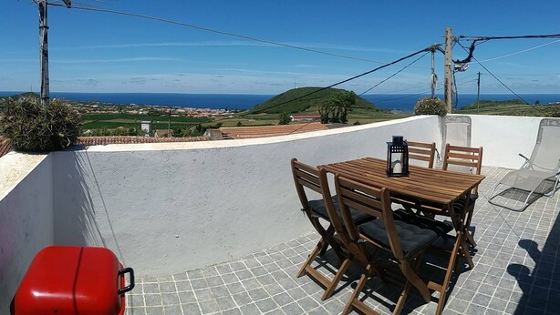 Una terrazza con tavolo e sedie, una valigia rossa e vista sul mare e sulle colline.