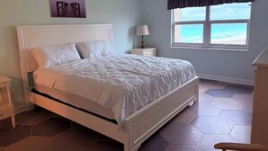 Ein Schlafzimmer mit Bett, Nachttisch, Lampe, einem Fenster mit Vorhängen und einem Deckenventilator.