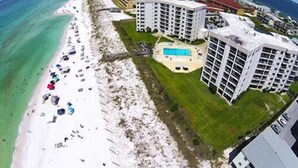 Luftaufnahme eines Küstenhotels mit mehreren Gebäuden, einem Strand mit Sonnenschirmen und einem Schwimmbad.