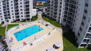 Ein Hochhaus mit Schwimmbecken, umgeben von Liegestühlen und Sonnenschirmen.
