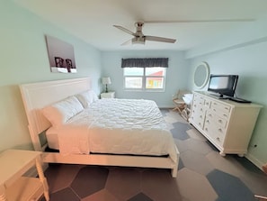 Un dormitorio con cama, cómoda, ventilador de techo, ventana y televisor.