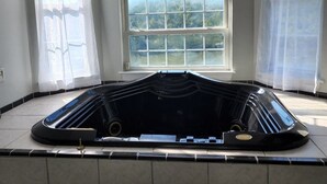 Una habitación con un amplio ventanal de arco, una bañera de hidromasaje negra y suelo de baldosas.