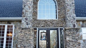Una casa de piedra con una entrada acogedora, un gran ventanal arqueado y una puerta decorativa.