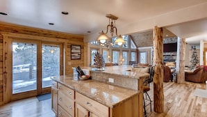 A spacious kitchen with wooden cabinetry, a granite countertop, and a large island. There is a stone fireplace and a Christmas tree in the background. - Log Home, Hot Tub & Pool-Table Game Room - 25 mi to Breckenridge (Fairplay)