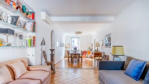 Un salon spacieux comprenant un grand canapé, une table à manger et une bibliothèque remplie de livres et d’objets décoratifs.