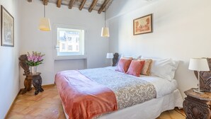 Une chambre avec un grand lit, des poutres en bois au plafond, une fenêtre et un vase rempli de fleurs.