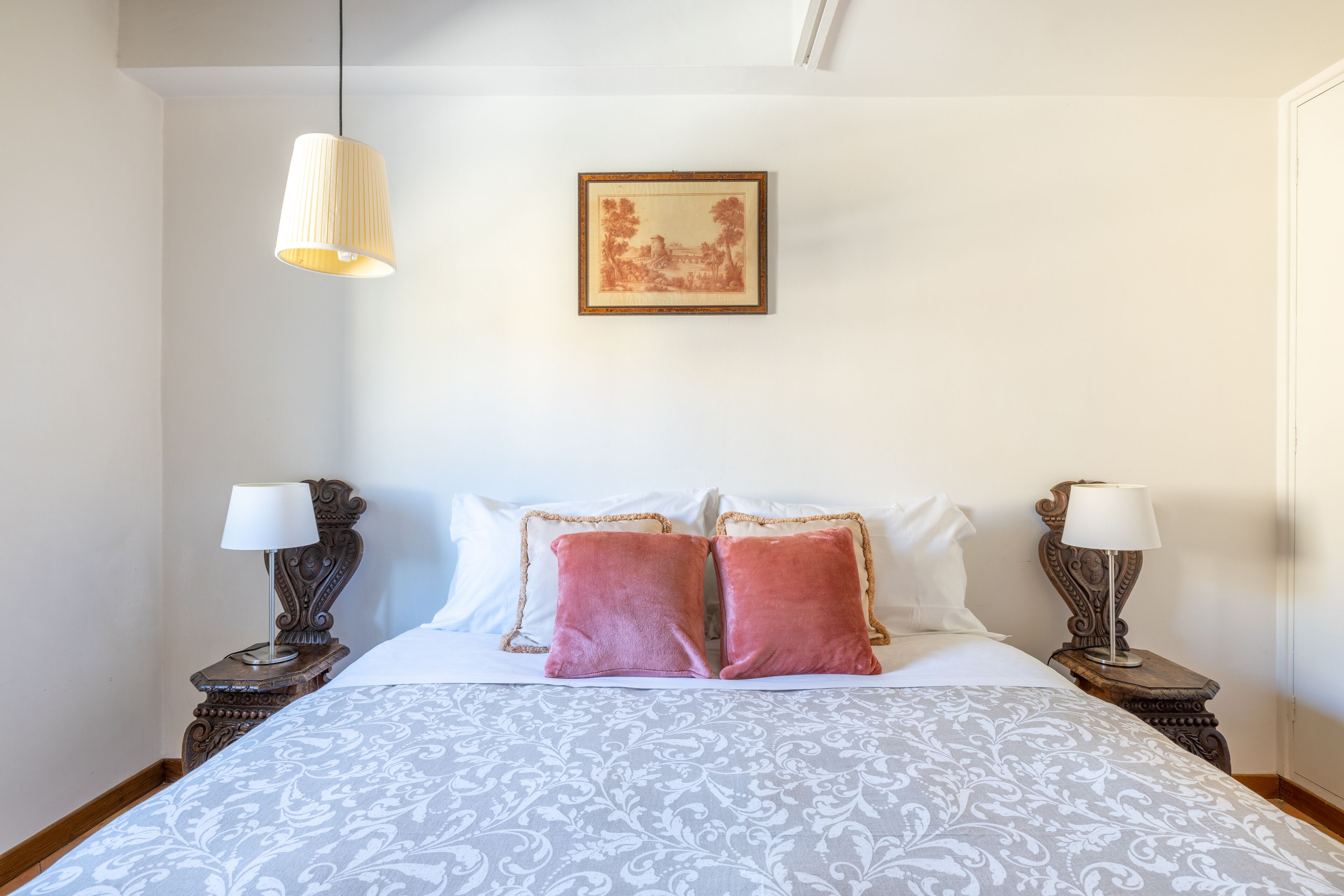 A neatly made bed with a patterned bedspread, two bedside lamps, and a framed picture on the wall.