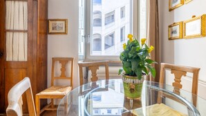 Une table ronde en verre, entourée de chaises, avec une plante en pot et des tableaux encadrés accrochés au mur.