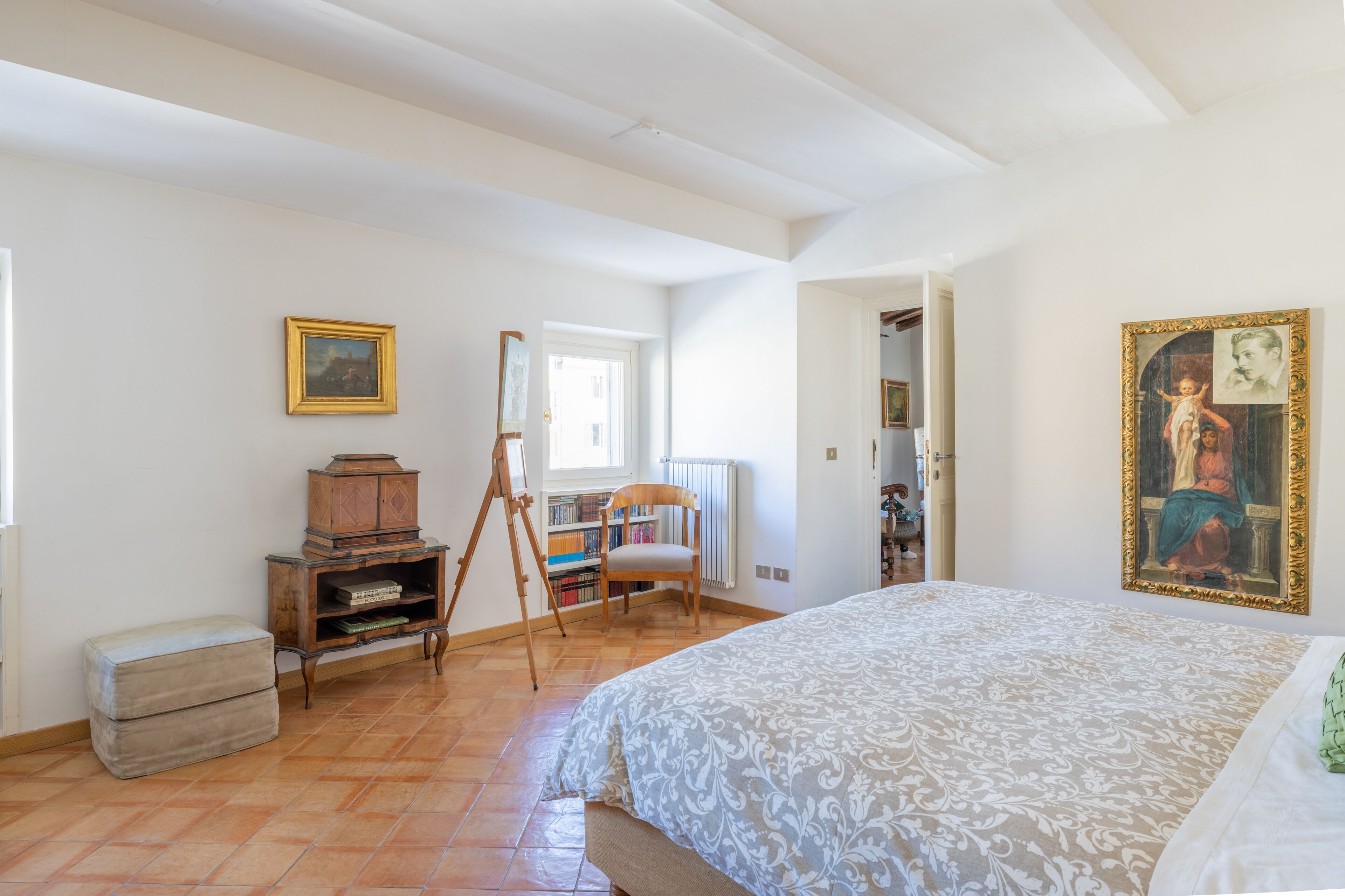 A bedroom with a large bed, a wooden cabinet, a chair, and a painting on the wall.