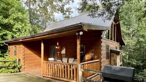 Een houten blokhut met een veranda, een barbecue en uitzicht op het omliggende bos.