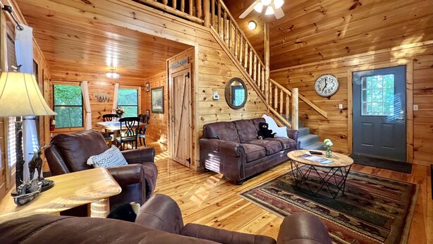 Een houten cabin met een wenteltrap, leren banken, een eethoek en een klok aan de muur.