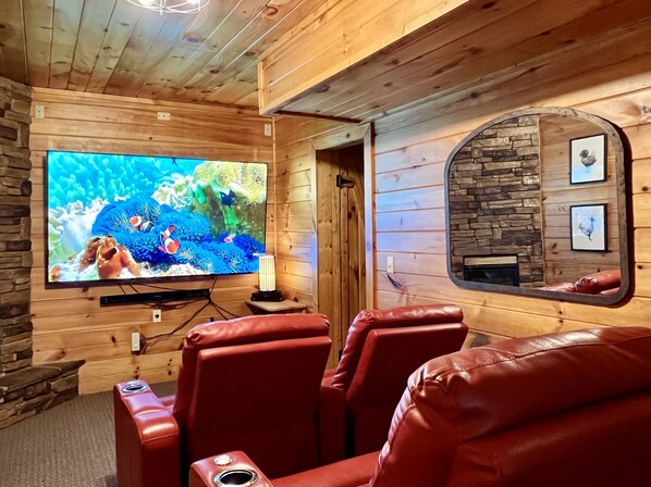 A cozy room with wooden walls and a large TV screen displaying an underwater scene. There are leather recliners and a stone fireplace. - 3 Fireplaces-86" TV theatre room-Nintendo Switch-Pool Table-Wifi-Dog friendly (Sevierville)