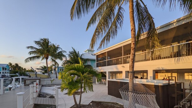 Un hotel moderno con zona de piscina, palmeras y una hamaca.