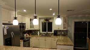 Una cocina con encimeras de granito, armarios blancos, electrodomésticos de acero inoxidable e iluminación colgante.