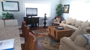 Una sala de estar con televisor, muebles de mimbre, un tapete floral y un sofá color beige.