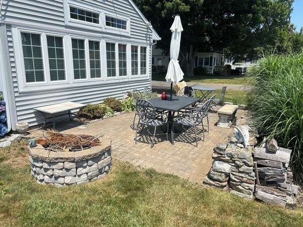 A patio with a stone table and chairs, a stone planter, and a white umbrella.