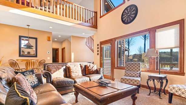 A spacious living room with a high ceiling, a staircase, and large windows.