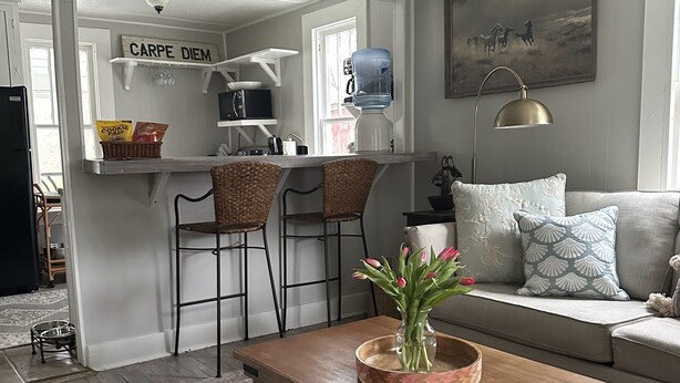A living room with a wooden coffee table, a sofa, a chandelier, and a kitchen area with a water dispenser and a sign reading "CARPE DIEM". - Peaceful Cottage Retreat Near Nashville! (Ashland City)
