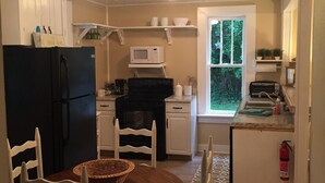 A compact kitchen with white cabinets, a black refrigerator, a microwave, and a small island with a sink. There is a window providing natural light and a view of greenery outside. - Peaceful Cottage Retreat Near Nashville! (Ashland City)