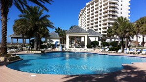 A swimming pool with lounge chairs and palm trees, surrounded by a building with multiple balconies. - Beach Club 3bd, 3ba. First floor on the beach. Super Special rate for Aug & Sept (Gulf Shores)