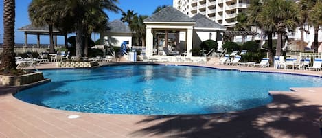A swimming pool with lounge chairs and palm trees, surrounded by a building with multiple balconies.