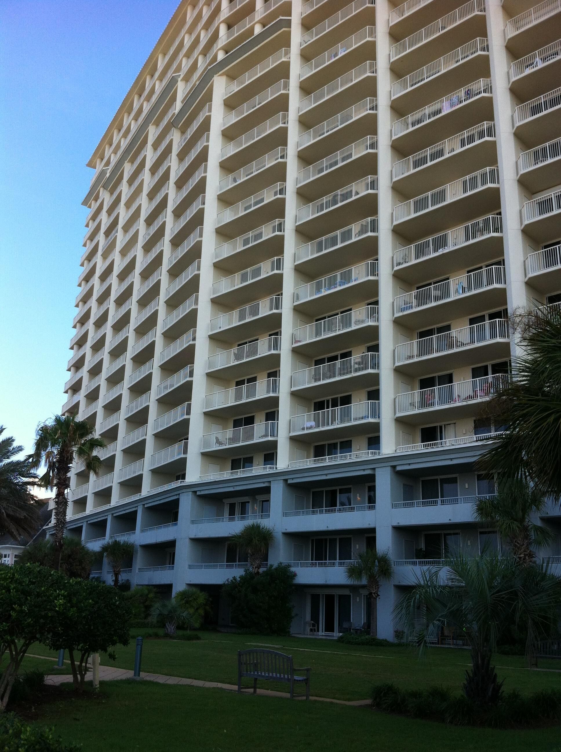 Un hotel moderno de gran altura con varios balcones, un patio central y abundante vegetación.