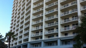 A high-rise hotel with multiple balconies, a central courtyard, and surrounding greenery. - Beach Club 3bd, 3ba. First floor on the beach. Super Special rate for Aug & Sept (Gulf Shores)
