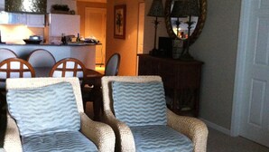 A living room with two wicker armchairs, a coffee table, and a dining area in the background. - Beach Club 3bd, 3ba. First floor on the beach. Super Special rate for Aug & Sept (Gulf Shores)