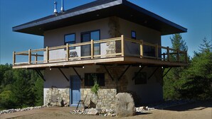 A two-story building with a stone facade, a balcony with a wooden railing, and a blue door. - Secluded Lookout Cabin- Fishing, ATV Trails, Canoe, Kayak & Campfires. (Shevlin)