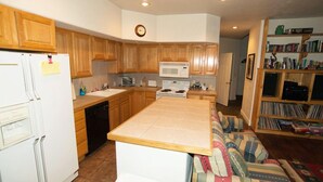 A kitchen with wooden cabinets, a microwave, stove, and a sink. There is a small island with a sink and a chair. A bookshelf with books is visible in the background. - 4 Br 3.5 baths Towne Home Driggs Idaho. Close to skiing, Jackson Hole, GTNP, YNP (Driggs)
