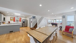 A spacious kitchen with a central island, a dining area with a wooden table and white chairs, and a view of the sea through large windows. - Waterfront Cottage on Lake Erie (Huron)